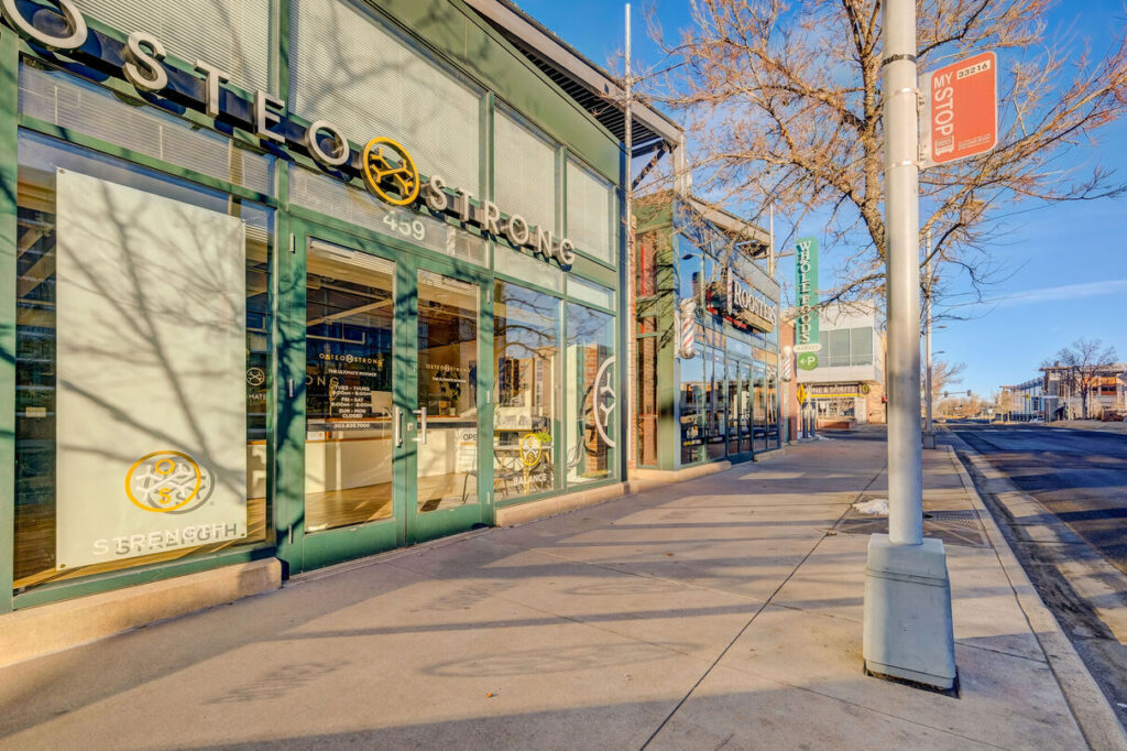 City sidewalk with several storefronts including Osteo Strong, Rooster's, and Whole Foods.