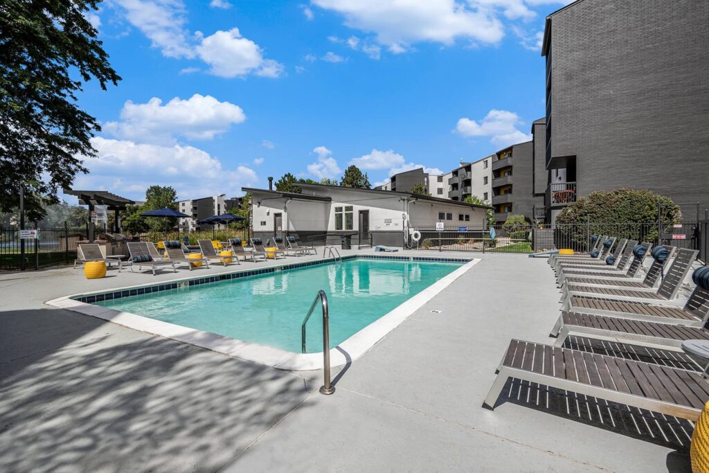Outdoor swimming pool surrounded by lounge chairs on a with apartment buildings in the background.