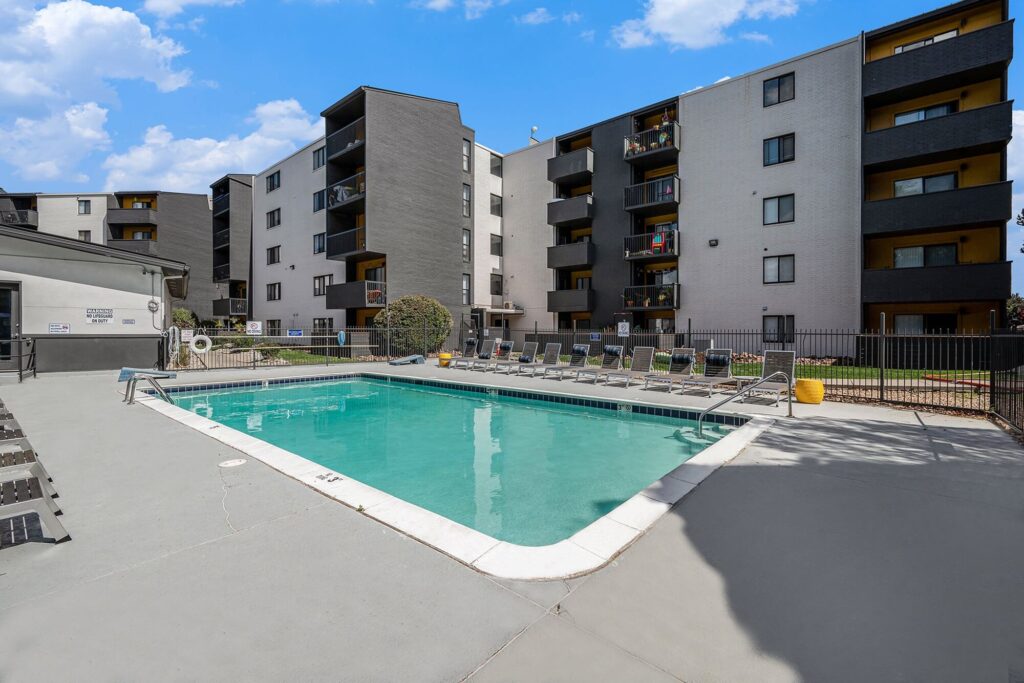 Apartment complex with an outdoor swimming pool, sun loungers, and modern apartment buildings in the background.